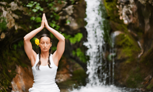 A girl doing yoga with hands up and a waterfall background